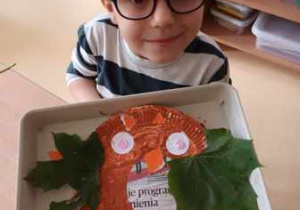 Chłopiec trzyma w dłoniach podkładkę ze swoją pracą plastyczną pt. "Sowa"
