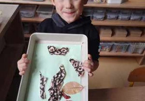 Chłopiec trzyma w dłoniach swoją kompozycję plastyczną pt. "Drzewo"