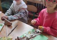 Dwie dziewczynki przy stoliku układają sylwetę drzewa z liści i elementów papieru