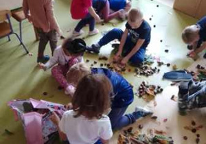 Dzieci w czasie zabawy sensorycznej układają sylwetę drzewa z materiału przyrodniczego