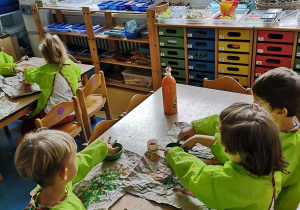 Dzieci siedzą przy stoliku i wykonują prace plastyczne