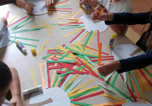 Dzieci starsze przyklejają kolorowe paski papieru, tworząc koronę drzewa