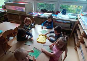 Grupa dzieci siedzi przy stoliku podczas wykonywania pracy plastycznej