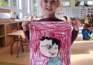 Dziewczynka trzyma w dłoniach namalowany przez siebie portret Marii Montessori