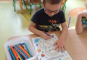 Chłopiec koloruje tematyczną kolorowankę przedstawiającą postać Marii Montessori
