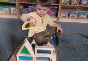 Chłopiec układa budowlę z drewnianych sensorycznych klocków