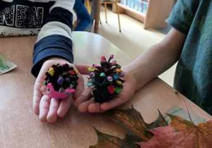 Zdjęcie prezentuje położone na dłoniach dzieci ślimaki zrobione z plasteliny oraz szyszek
