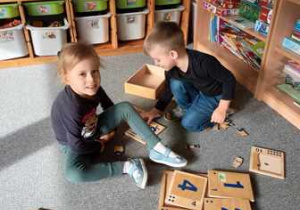 Dziewczynka i chłopiec układają drewniane puzzle przedstawiające graficzny zapis cyfr