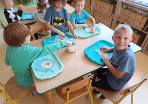 Dzieci siedzą przy stoliku, w czasie wykonywania pracy plastycznej pt. "Nadmorski obrazek" ugniatają masę solną i posypują uformowany element piaskiem