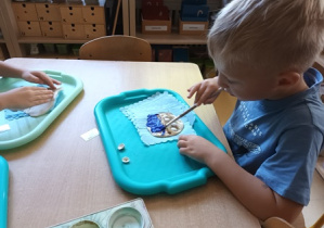 Chłopiec rozprowadza farbę w kolorze niebieskim na powierzchni masy solnej przy użyciu pędzla