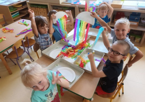 Dzieci starsze przy stoliku wykonują pracę plastyczną wykorzystaniem talerzyka papierowego oraz kolorowych pasków bibuły