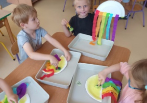 Dzieci w czasie wykonywania pracy plastycznej pt. "Tęcza" stemplują żółtą farbą powierzchnię papierowego talerzyka