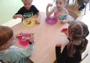 Dzieci siedzą przy stoliku i jedzą tort urodzinowy