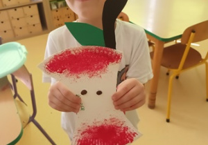 Chłopiec trzyma w dłoniach zrobioną przez siebie pracę plastyczną przedstawiającą ogryzek od jabłka