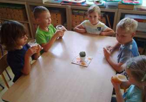 Zdjęcie przedstawia dzieci siedzące przy stoliku i pijące sok jabłkowy