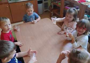 Dzieci siedzą przy stoliku i piją własnoręcznie zrobiony sok jabłkowy