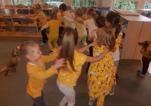 Dzieci ubrane na żółto podczas zabawy ruchowej stoją ustawione w pociągu, jedno za drugim