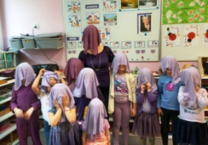 Dzieci wraz z panią stoją obok siebie i mają założone na głowy fioletowe chustki