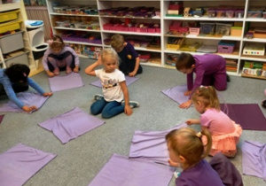 Dzieci siedzą na dywanie i mają rozłożone przed sobą fioletowe chustki