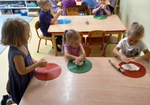 Dzieci siedzą przy stolikach i wykonują indywidualną pracę z masą solną
