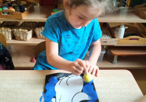 dziewczynka stempluje gąbką umoczoną w farbie sylwetę pingwina