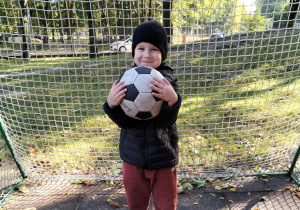 chłopiec stoi przy bramce i trzyma piłkę