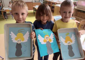 Chłopcy trzymają w dłoniach podkładki ze swoimi pracami plastycznymi przedstawiającymi anioły