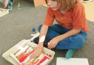 Chłopiec siedzi na dywanie o dokleja paski białego papieru do swojej pracy plastycznej