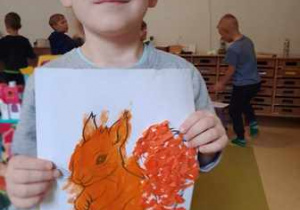 Chłopiec trzyma w dłoniach wykonaną przez siebie pracę plastyczną pt. "Wiewiórka"