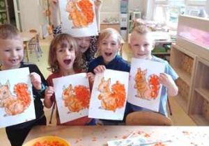 Grupa dzieci pozuje do zdjęcia z pracami plastycznymi przedstawiającymi wiewiórkę