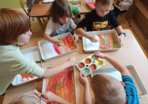 Dzieci starsze malują temperami w jesiennych kolorach tło pracy plastycznej