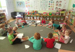 Dzieci siedzą na dywanie w kręgu i wydzierają paski papieru do pracy plastycznej pt. "Jesienne brzozy"