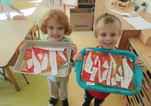 Tadzio i Natan pozują do wspólnego zdjęcia z wykonanymi przez siebie pracami plastycznymi przedstawiającymi jesienne brzozy