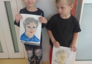 Chłopiec i dziewczynka prezentują wykonane przez siebie portrety Marii Montessori