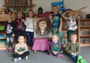 Dzieci pozują do zdjęcia stojąc obok portretu Marii montessori