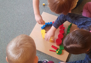 Dzieci układają ślimaka z kolorowych cylindrów na drewnianej tabliczce