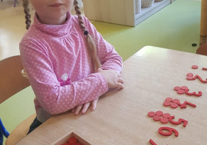 Dziewczynka siedzi przy stoliku i układa cyfry i czerwone żetony