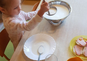 Dziewczynka nalewa mleko z wazy do talerza