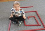 Chłopiec siedzi na dywanie w środku labiryntu ułożonego z czerwonych sztang