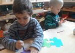 dwóch chłopców siedzi przy stoliku i ozdabia kolorowe puzzle