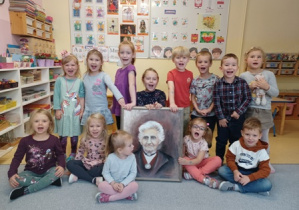 Dzieci pozują siedząc lub stojąc obok portretu Marii Montessori