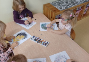 Dzieci siedzą przy stoliku i rysują portrety Marii Montessori