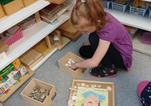 Dziewczynka ozdabia kolorowymi kamykami portret Marii Montessori leżący na korkowej podkładce