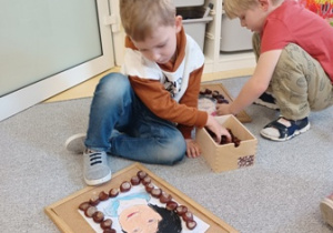 Chłopiec ozdabia portret Marii Montessori ułożony na korkowej podkładce