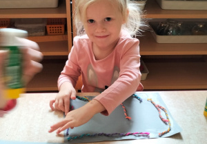 dziewczynka przykleja włóczkę tworząc abstrakcyjny obraz