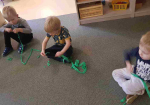 Dzieci siedzą na dywanie i drą bibułę na kawałki