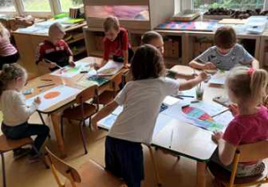 Dzieci przy stoliku w czasie pracy plastycznej "Jesienny liść" malują farbami akwarelowymi na dużych arkuszach papieru