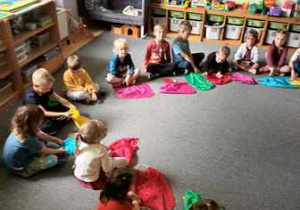Dzieci siedzą na dywanie z kolorowymi chustkami w czasie zabawy muzycznej "Jesień"