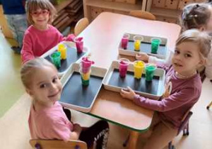 Dziewczynki siedzą przy stole w czasie wykonywania przestrzennej pracy plastycznej pt. "Sygnalizacja świetlna"