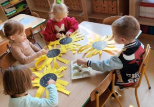 Dzieci siedzą przy stoliku i przyklejają żółte płatki słonecznika